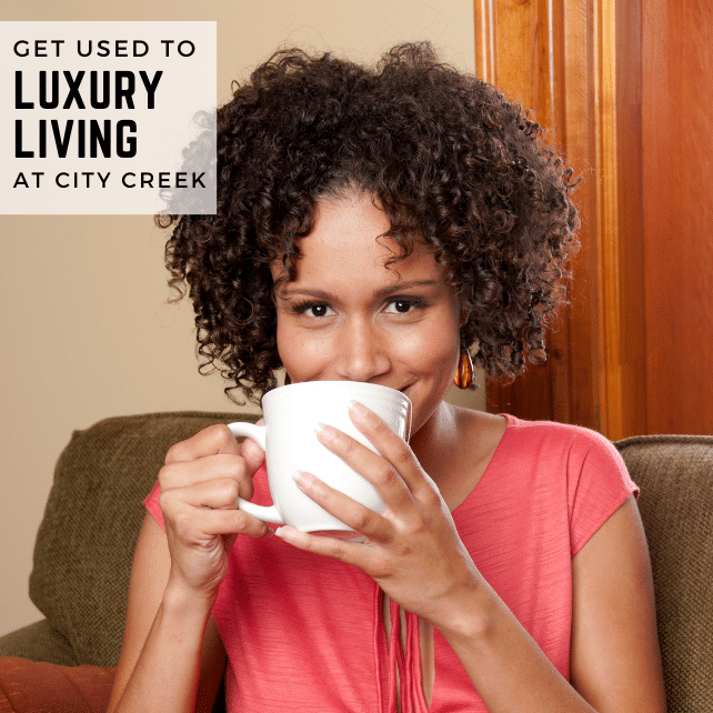 A woman drinking from a white cup with the words, Get used to luxury living at City Creek.